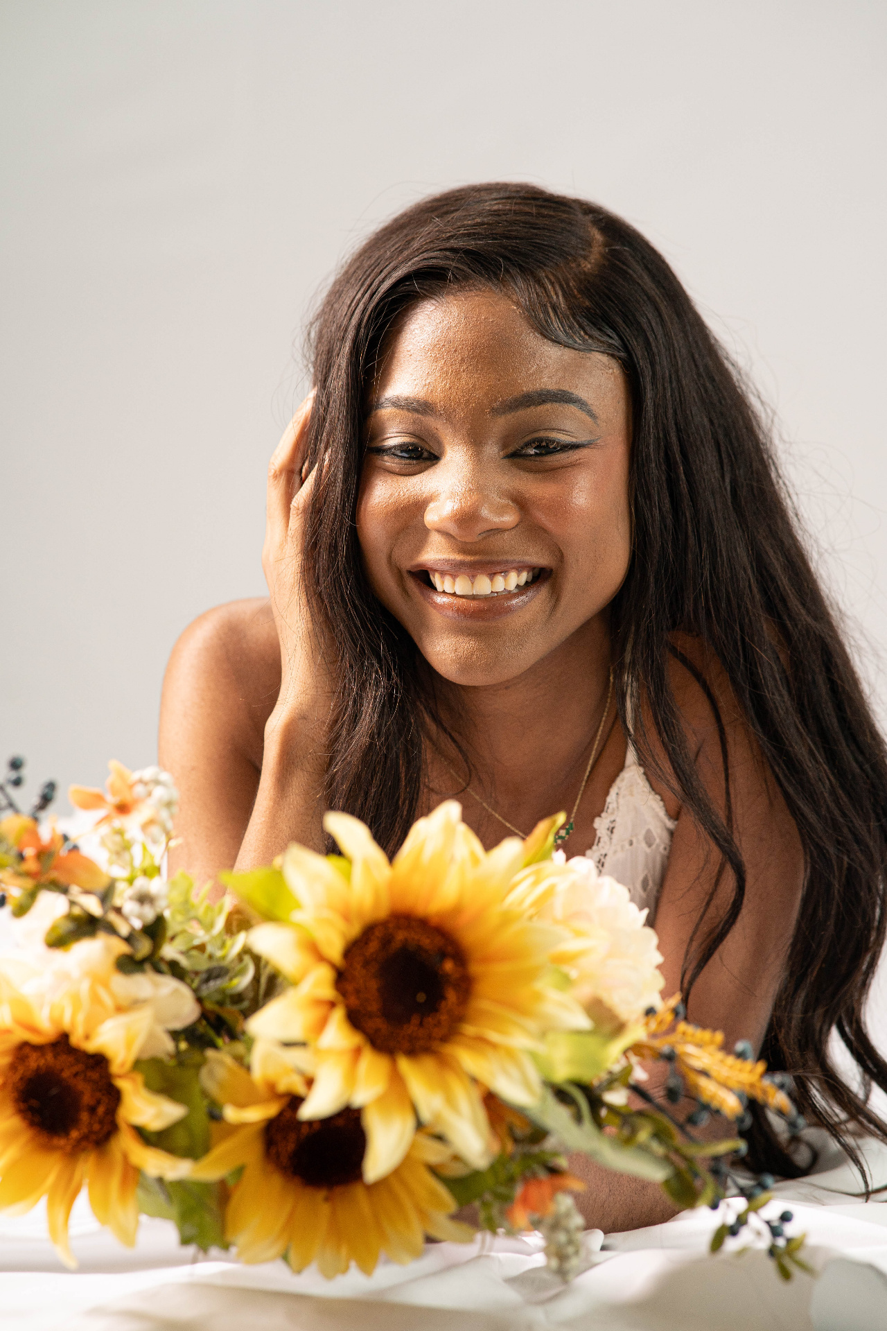 Commercial lifestyle frame of Chelsey Moné laughing beside a sunflower bouquet on a white set
