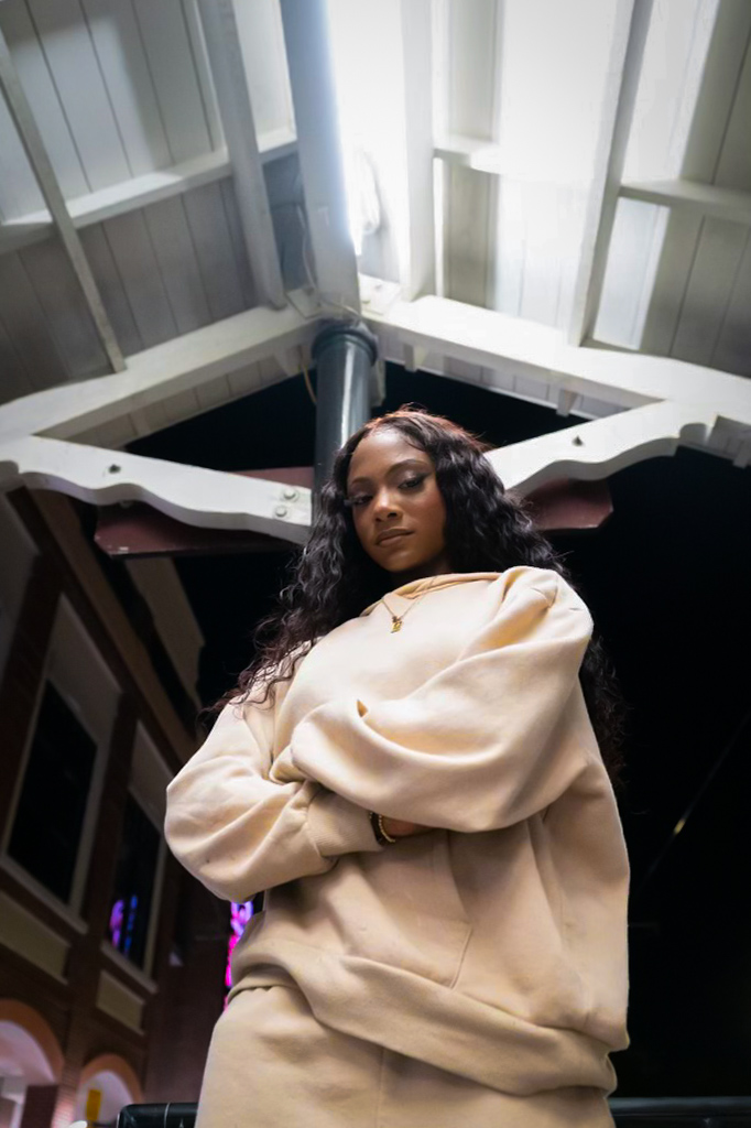 Editorial frame of Chelsey Moné in an oversized cream hoodie against white architecture