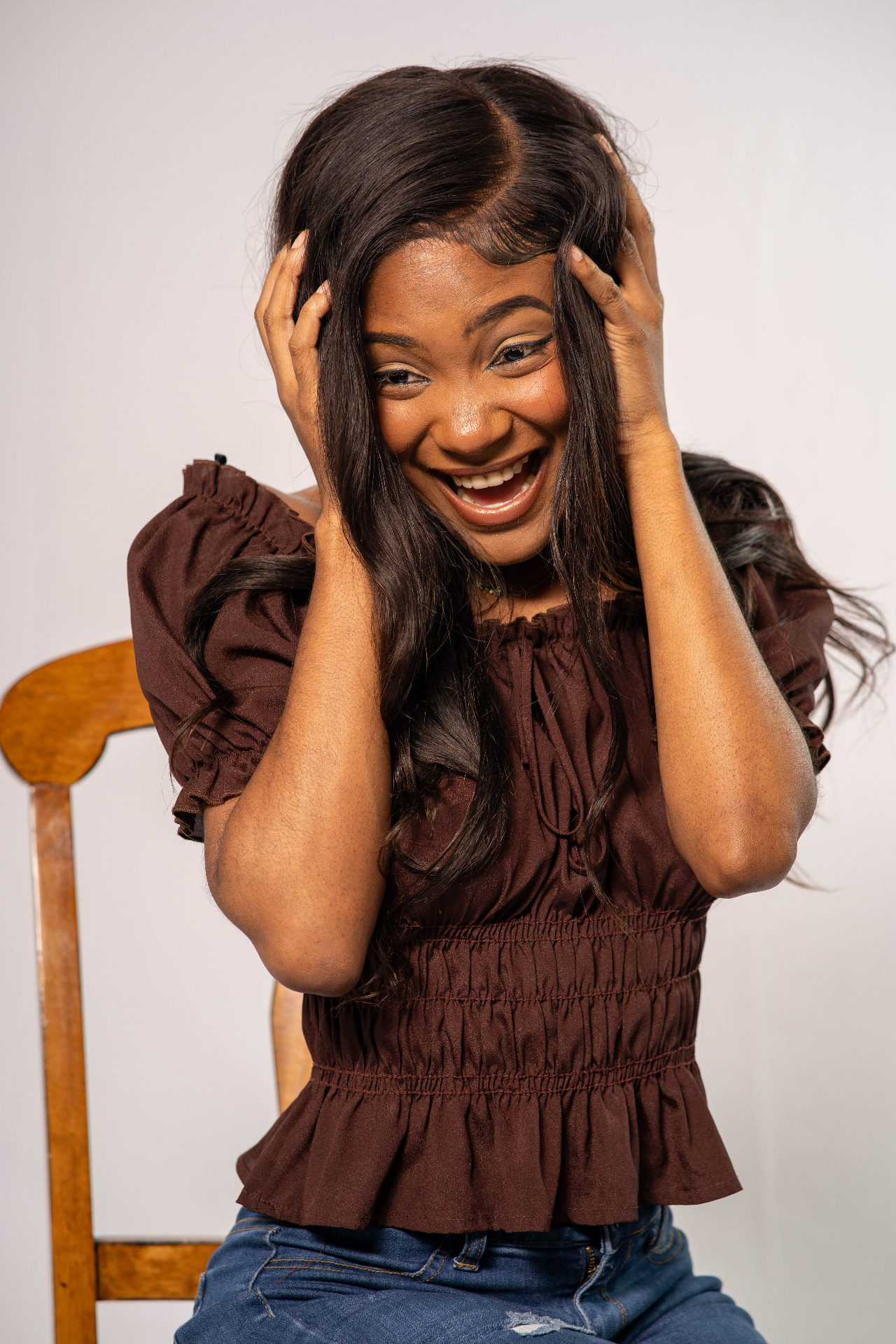 Commercial studio frame of Chelsey Moné laughing with hands in her hair, wearing a brown off-shoulder blouse and denim