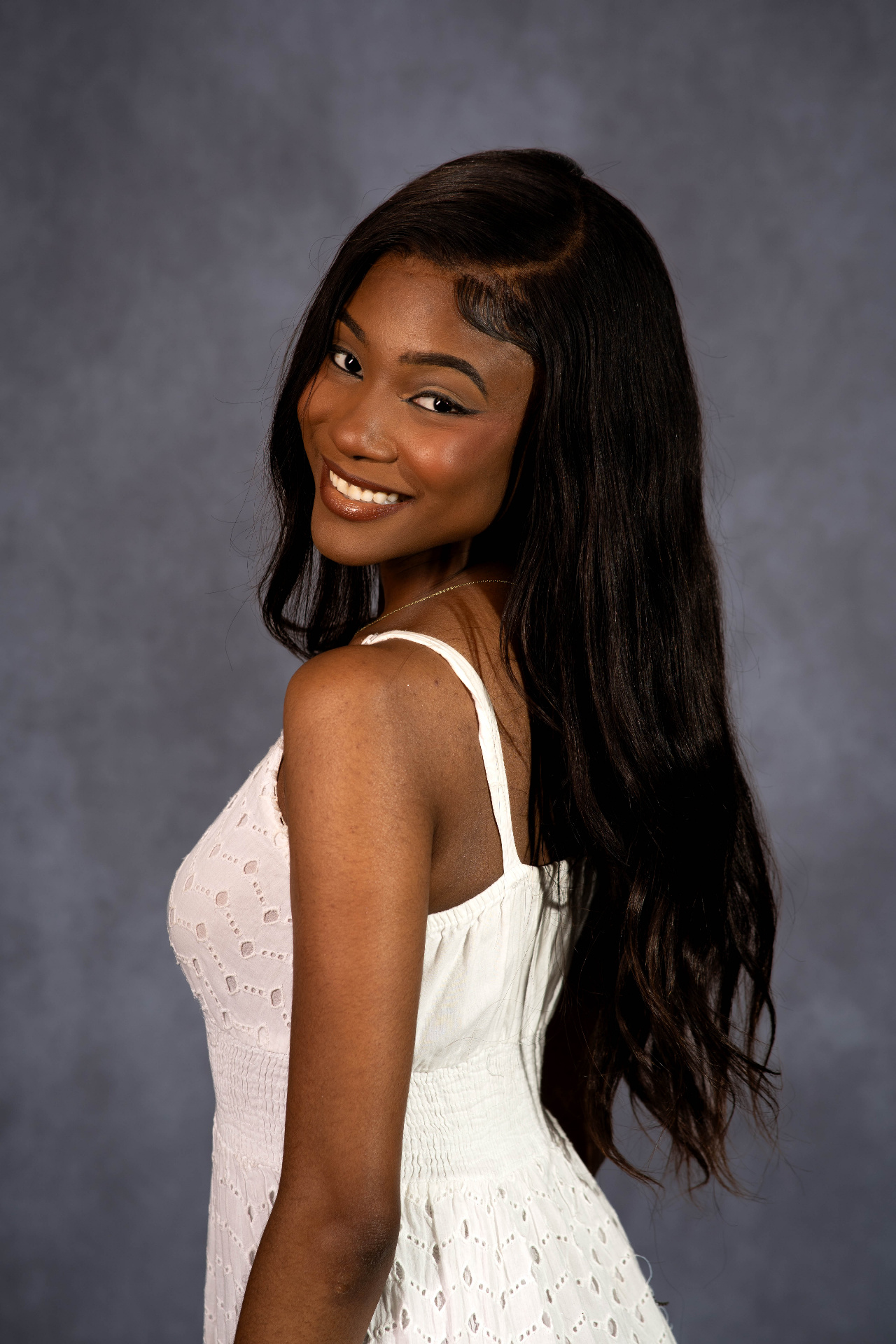 Studio over-the-shoulder profile portrait of Chelsey Moné smiling in a white dress