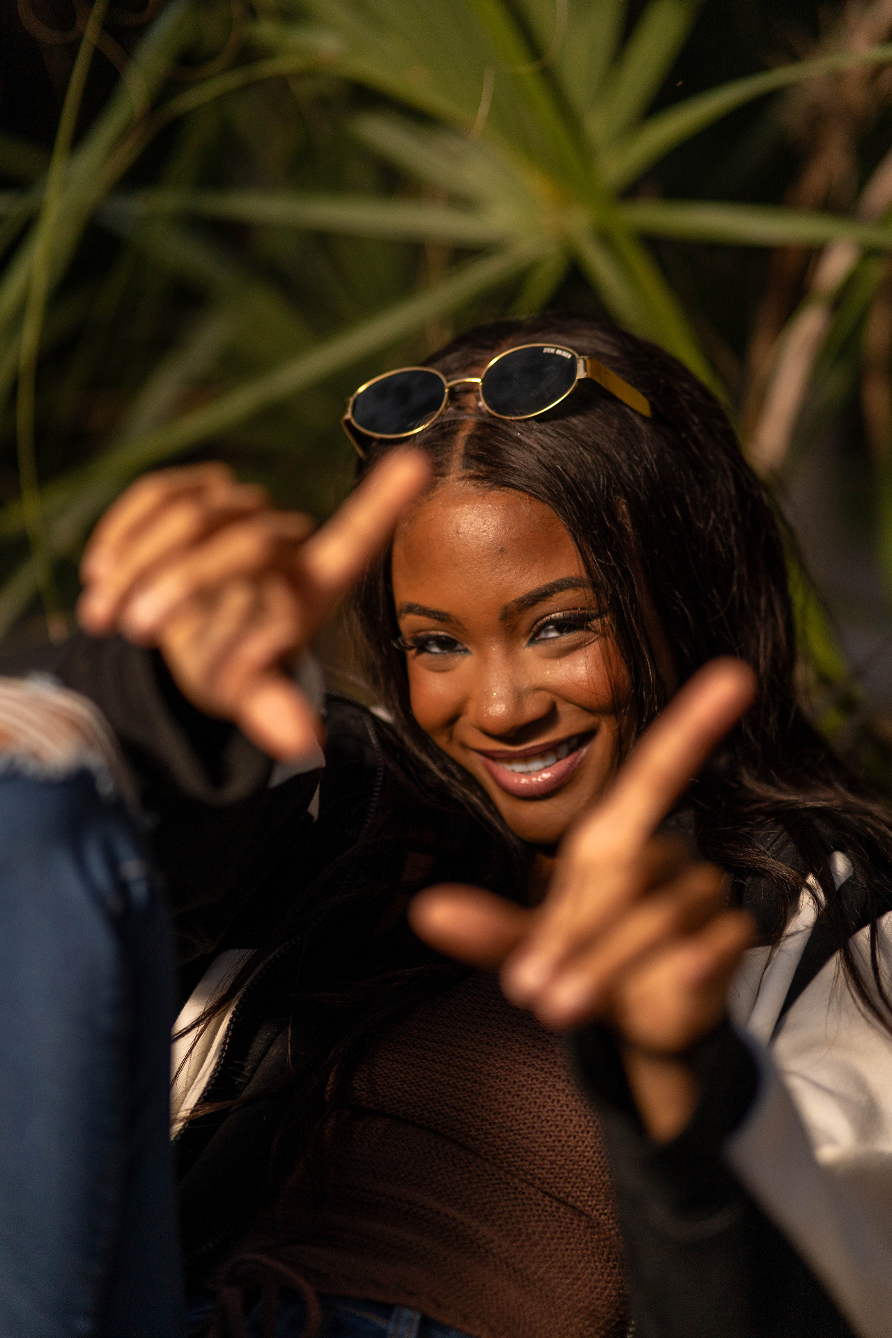 Playful lifestyle frame of Chelsey Moné framing the camera with her hands under palm fronds